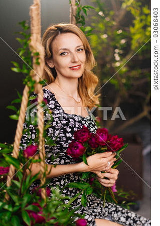 an attractive middle-aged blonde woman with flowers sits on a swing. 93068403