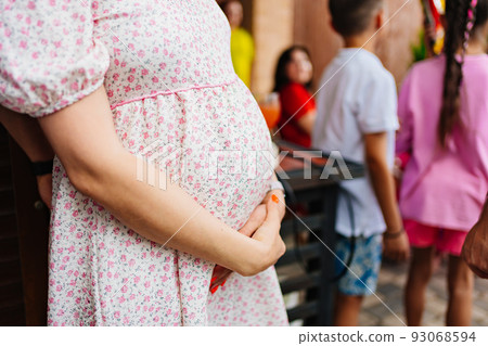 a pregnant woman in a summer dress strokes her stomach. 93068594