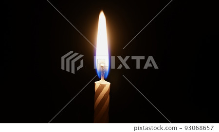 a small striped candle with flames in the dark.  93068657