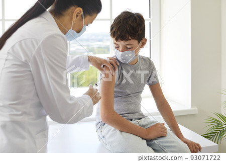 Nurse or doctor at clinic giving vaccine to little school child in medical face mask 93071722