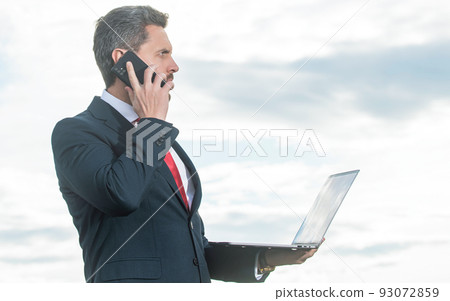 businessman in suit speaking on phone and hold laptop 93072859
