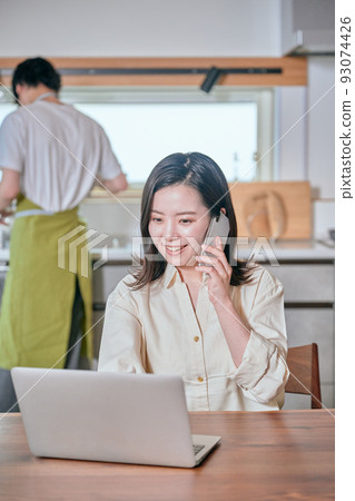 A woman who makes a phone call on a smartphone in telework and a man who does housework A woman who makes a phone call on a smartphone in telework and a man who does housework 93074426