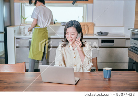 A woman who makes a phone call on a smartphone in telework and a man who does housework A woman who makes a phone call on a smartphone in telework and a man who does housework 93074428