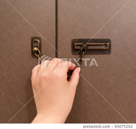 female hand closes the door on a bronze chain female hand closes the door on a bronze chain 93075202