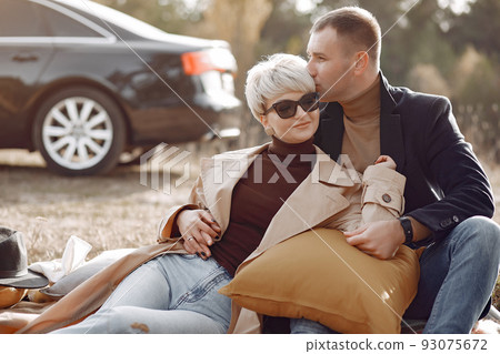Couple in a field. Girl in a brown coat. Man with his wife near the car Couple in a field. Girl in a brown coat. Man with his wife near the car 93075672