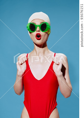 A shocked unusual swimmer in glasses holds the straps of a swimsuit posing on a blue background. Art fashion concept 93076151