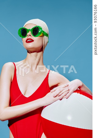 Let's go on vacation. A happy woman in stylish glasses poses with a swimming ball looking away . Stylish portrait on a blue background Let's go on vacation. A happy woman in stylish glasses poses with a swimming ball looking away . Stylish portrait on a blue background 93076166