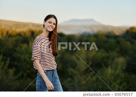 A young woman laughs and looks at the camera in simple clothes against the backdrop of a beautiful landscape of mountains and trees in autumn. Lifestyle on the move 93076557