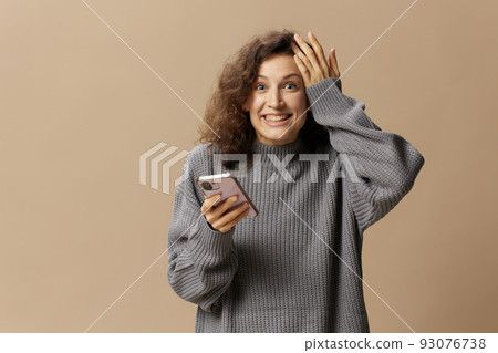 Overjoyed lucky curly cute lady in gray casual sweater get cool news from message posing isolated on over beige pastel background. Social media, network, distance communication concept. Copy space Overjoyed lucky curly cute lady in gray casual sweater get cool news from message posing isolated on over beige pastel background. Social media, network, distance communication concept. Copy space 93076738