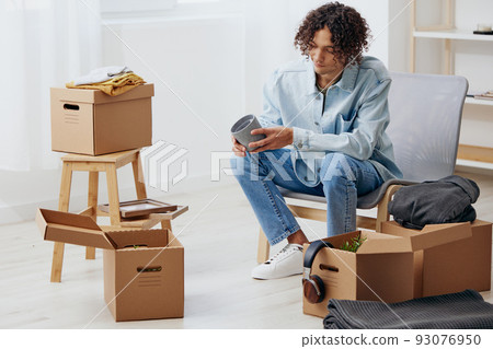 A young man unpacking things from boxes in the room sorting things out A young man unpacking things from boxes in the room sorting things out 93076950