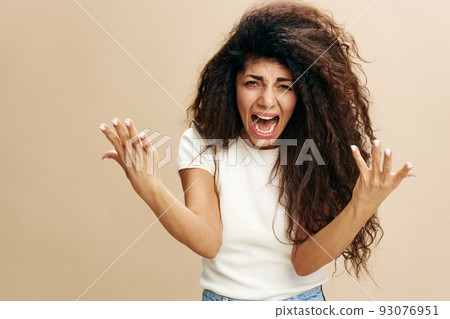 Crying beautiful Latin female in basic white t-shirt with afro hold hands up, scream at camera. Scandal concept. Studio shoot over pastel beige background. Copy space, free place for design ad Crying beautiful Latin female in basic white t-shirt with afro hold hands up, scream at camera. Scandal concept. Studio shoot over pastel beige background. Copy space, free place for design ad 93076951