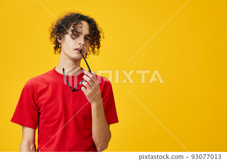 Incredulous myopic young student man in red t-shirt hold funny eyewear on teeth posing isolated on yellow studio background. The best offer with free place for advertising. Education College concept Incredulous myopic young student man in red t-shirt hold funny eyewear on teeth posing isolated on yellow studio background. The best offer with free place for advertising. Education College concept 93077013
