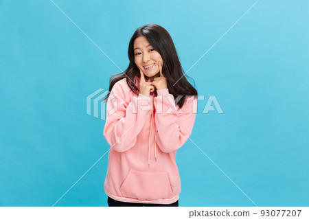Happy lovely Asian student young lady in pink hoodie sweatshirt smiling posing isolated on over blue studio background. The best offer for ad. People Emotions for Everyday concept Happy lovely Asian student young lady in pink hoodie sweatshirt smiling posing isolated on over blue studio background. The best offer for ad. People Emotions for Everyday concept 93077207