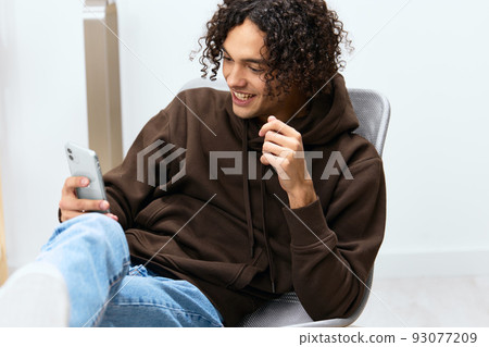 A young man sitting on a chair with a phone communication interior isolated background 93077209