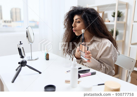 Funny tanned handsome curly Latin beauty blogger in linen shirt teach how to do cheekbones in home white interior. Copy space Mockup Banner. Influencer record video review blog using smartphone Funny tanned handsome curly Latin beauty blogger in linen shirt teach how to do cheekbones in home white interior. Copy space Mockup Banner. Influencer record video review blog using smartphone 93077758