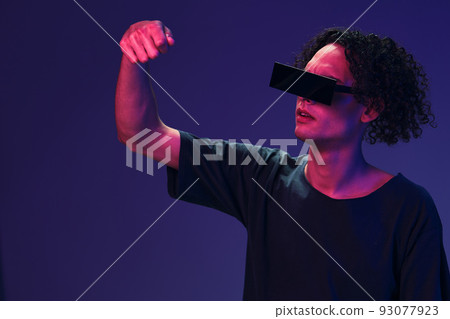 Excited stylish tanned curly man in black t-shirt eyewear holds invisible object posing isolated on color pink blue background. Cool fashion offer. Virtual Reality New Collection concept. Copy space Excited stylish tanned curly man in black t-shirt eyewear holds invisible object posing isolated on color pink blue background. Cool fashion offer. Virtual Reality New Collection concept. Copy space 93077923