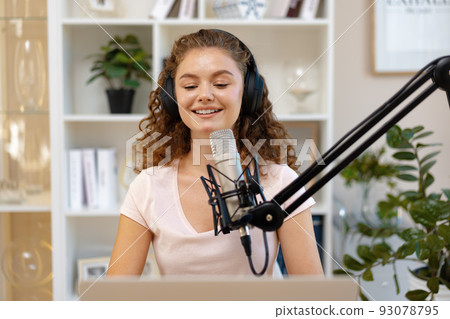 Young curly female recording podcast from home and talking into a microphone Young curly female recording podcast from home and talking into a microphone 93078795