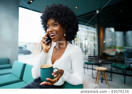 Smiling young african woman talking on cellphone at cafe Smiling young african woman talking on cellphone at cafe 93079138