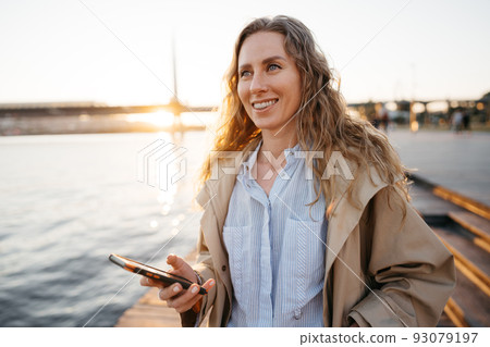 Handsome young smiling woman with mobile phone walking on the street Handsome young smiling woman with mobile phone walking on the street 93079197