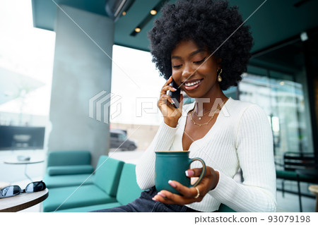 Smiling young african woman talking on cellphone at cafe 93079198