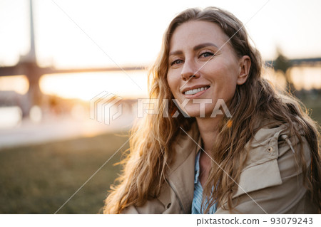 Happy young woman sitting on lawn outdoors in the city Happy young woman sitting on lawn outdoors in the city 93079243