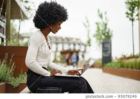 Young african american businesswoman working using laptop sitting on the bench in the city Young african american businesswoman working using laptop sitting on the bench in the city 93079249