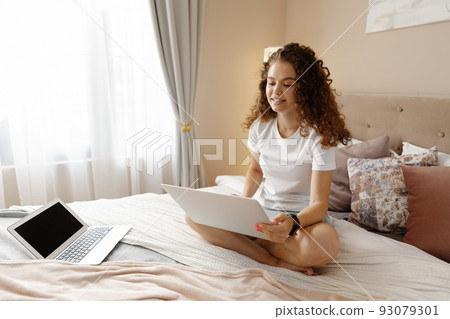 Portrait of a young curly woman using laptop in bed at home 93079301