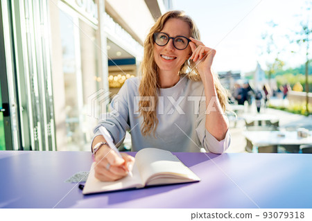 Casual woman sitting at table and taking notes in notebook .on the cafe terrace Casual woman sitting at table and taking notes in notebook .on the cafe terrace 93079318