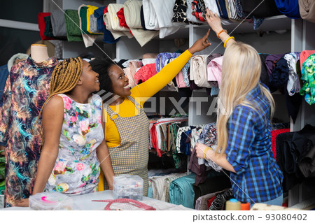 The clothing designer shows her customers the fabrics on the rack. 93080402