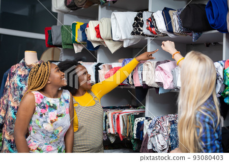 Dark-skinned customers choose the fabrics the seamstress shows them. Dark-skinned customers choose the fabrics the seamstress shows them. 93080403