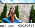 Attractive young fitness girl looking at her smart phone sitting on a pilates ball outdoors. girl exercising while sharing it on her social networks. health and wellness concept. 93080618