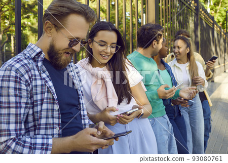 Happy young diverse people standing on city street and using their mobile phones Happy young diverse people standing on city street and using their mobile phones 93080761