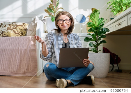 Mature woman sitting on the floor at home looking at laptop Mature woman sitting on the floor at home looking at laptop 93080764