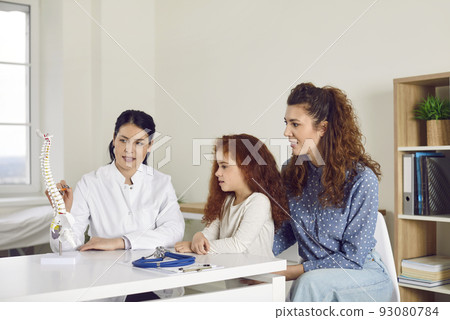Doctor at orthopedic clinic talking to mother and child and showing anatomical spine model 93080784
