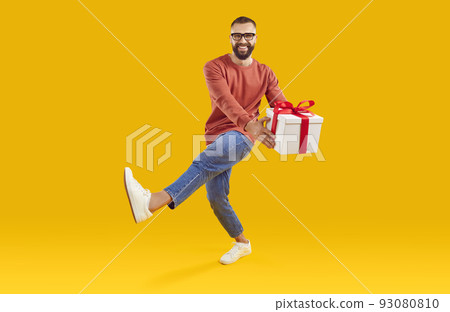 Portrait of happy smiling young man with gift box dancing on yellow studio background Portrait of happy smiling young man with gift box dancing on yellow studio background 93080810
