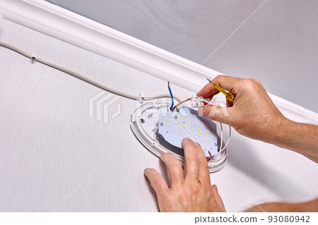 Installing LED wall light fixture, electrician connect connecting wires to home electrical wiring. 93080942