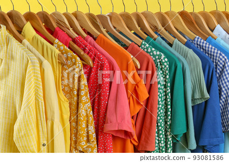 Bright clothes on hangers against yellow background, closeup. Rainbow colors Bright clothes on hangers against yellow background, closeup. Rainbow colors 93081586
