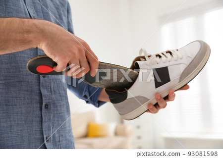 Man putting orthopedic insole into shoe at home, closeup 93081598