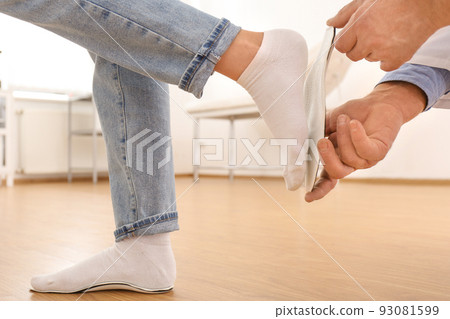 Male orthopedist fitting insole on patient's foot in clinic, closeup Male orthopedist fitting insole on patient's foot in clinic, closeup 93081599