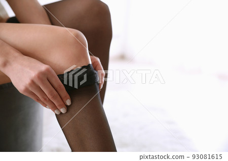 Beautiful woman putting on stocking indoors, closeup Beautiful woman putting on stocking indoors, closeup 93081615