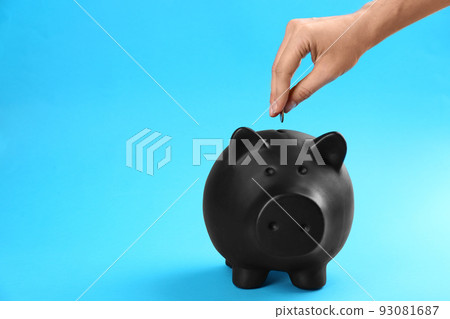 Woman putting coin into piggy bank on blue background, closeup Woman putting coin into piggy bank on blue background, closeup 93081687