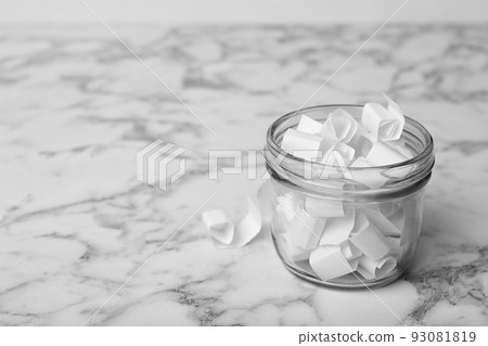 Glass jar with paper pieces on white marble table, space for text 93081819