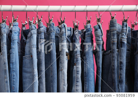 Rack with stylish jeans on pink background, closeup Rack with stylish jeans on pink background, closeup 93081959