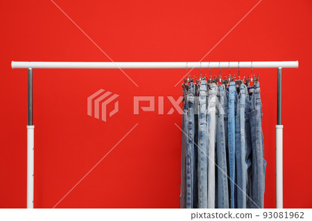 Rack with stylish jeans on red background 93081962