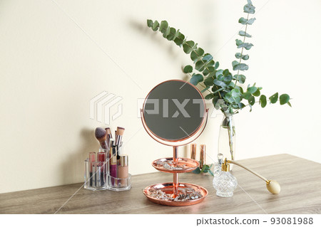 Mirror with jewelry and makeup products on wooden table near light wall Mirror with jewelry and makeup products on wooden table near light wall 93081988