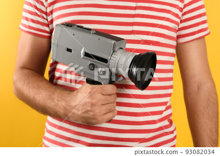 Man with vintage video camera on yellow background, closeup Man with vintage video camera on yellow background, closeup 93082034