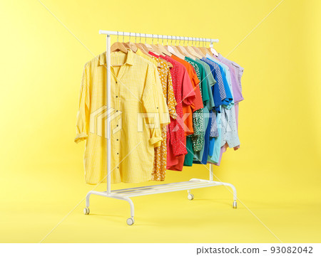 Bright clothes hanging on rack against yellow background. Rainbow colors 93082042