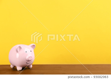 Pink piggy bank on wooden table against yellow background. Space for text 93082063
