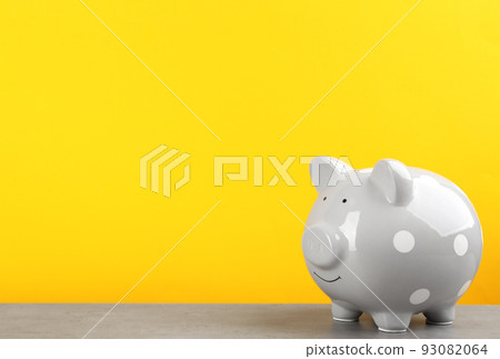Grey piggy bank on light grey table against yellow background. Space for text 93082064