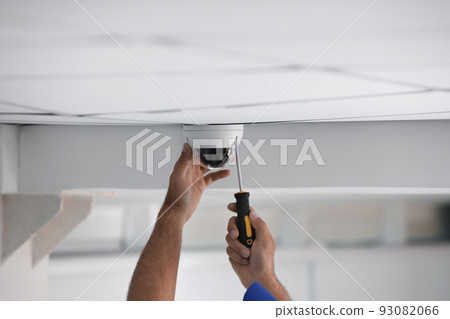 Technician installing CCTV camera on ceiling indoors, closeup 93082066